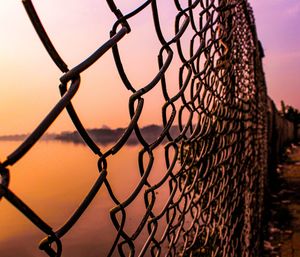 Close-up of chainlink fence against sky during sunset