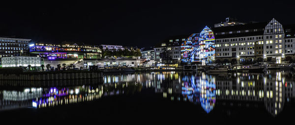 Illuminated buildings by river against sky at night