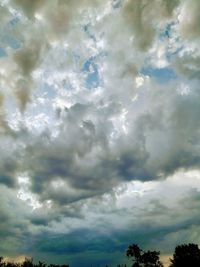 Low angle view of trees against cloudy sky