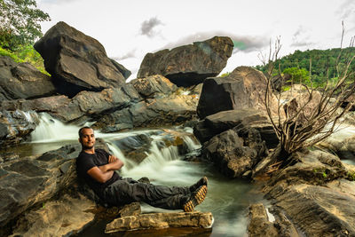 Portrait of man sitting on rock against sky