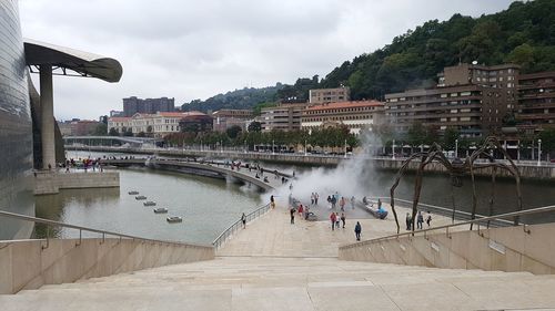 People on bridge over river in city against sky