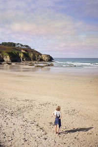 Rear view of boy walking on beach against sky