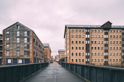 Empty footbridge by buildings against sky