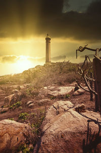 Lighthouse amidst rocks and buildings against sky