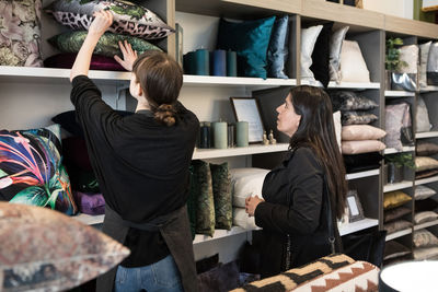 Mature female customer looking at young owner holding cushion in rack