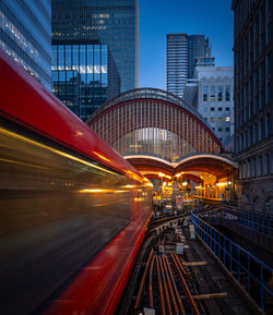 A vibrant red london underground subway train is traveling through bustling city during night hours