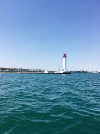 Lighthouse by sea against clear sky