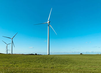 Wind turbines on field against blue sky