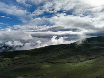 Scenic view of grassy mountain against cloudy sky