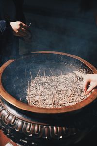 High angle view of woman holding incense stick standing by container at temple