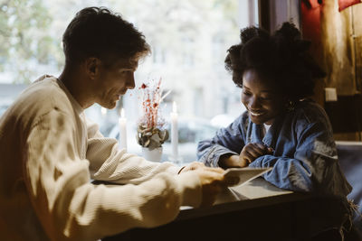 Boyfriend suggesting dish to girlfriend looking at menu card in restaurant