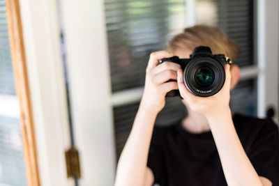 Young person holding up modern camera in front of face in doorway