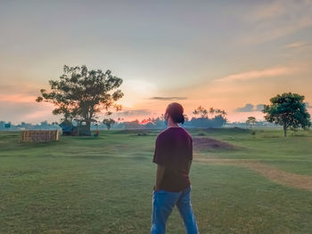 Rear view of man standing on field against sky during sunset