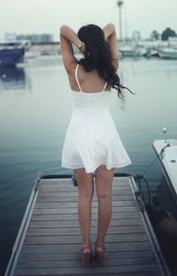 Rear view of woman with hands in hair standing on pier