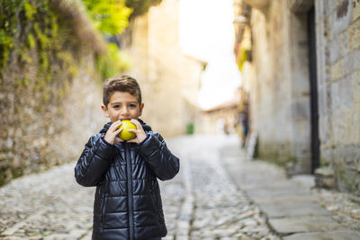 Portrait of smiling boy eating apple while standing on street
