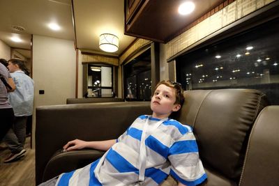 Boy looking away while sitting on seat in illuminated room