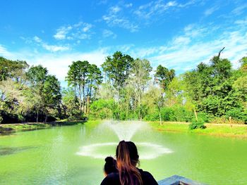 Rear view of mother and daughter by fountain against sky