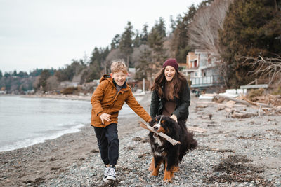 Cheerful mother and son with dog carrying wood in mouth at beach