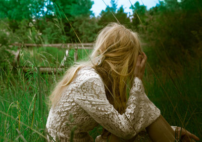 Woman sitting on field against trees