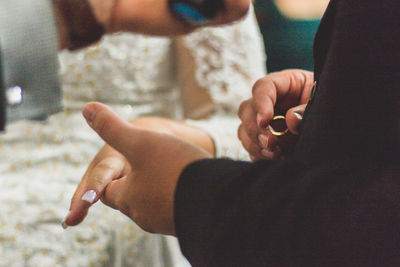 Midsection of groom exchanging ring with bride