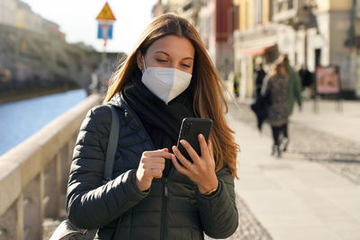 Woman wearing mask using phone on street