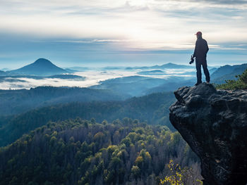 Man standing on rock looking at mountains against sky