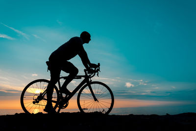 Silhouette man riding bicycle against sky during sunset