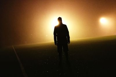 Rear view of silhouette man walking on illuminated road at night