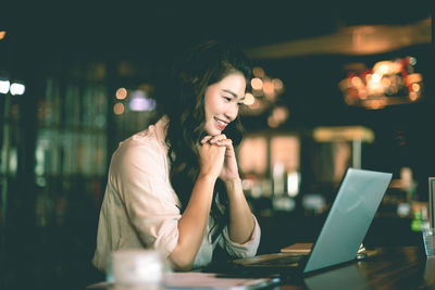 Full length of young woman using phone while sitting at table