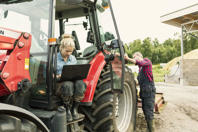 Woman using laptop while man standing by tractor