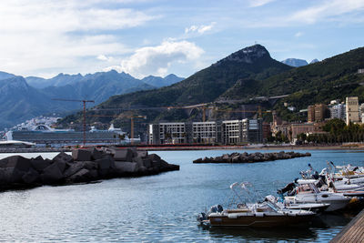 Sailboats in sea by buildings and mountains against sky