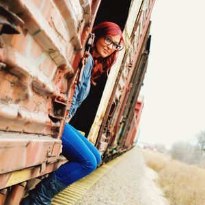 Smiling young woman sitting in freight train against clear sky