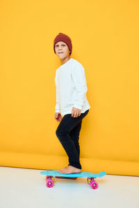 Portrait of young woman standing against yellow background