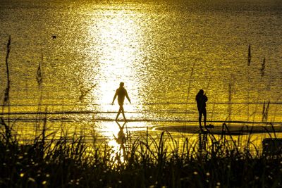 Silhouette people by sea against sky during sunset