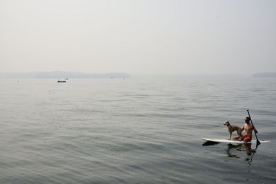 Shirtless man paddleboarding with dog on sea against sky