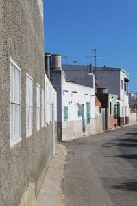 Footpath amidst buildings in town against clear blue sky