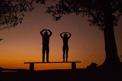 Silhouette people standing by tree against orange sky