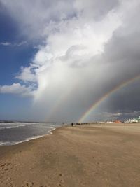 Scenic view of beach against rainbow in sky