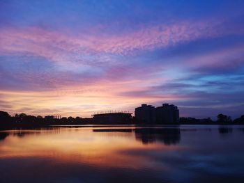 Silhouette buildings by lake against sky during sunset