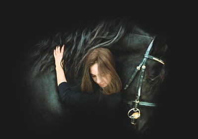 Digital composite image of woman embracing horse against black background