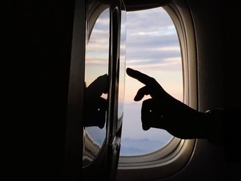 Cropped image of silhouette hand touching device screen in airplane