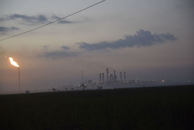 Fire emitting from smoke stack at industrial site against sky