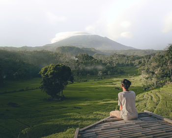 Rear view of man sitting on mountain against sky