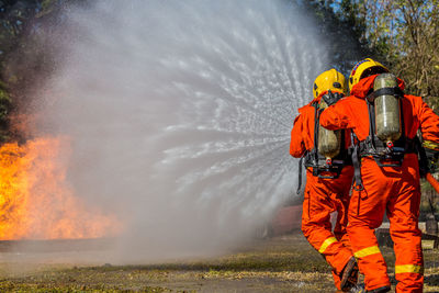 Rear view of firefighters spraying water on field
