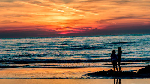 Silhouette man standing on beach against sky during sunset