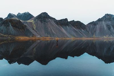 Man standing on frozen lake by mountains against sky