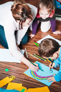 High angle view of mother and children painting on paper at home