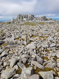 Rocks strewn across summit of glyder fawr with rock formation like a ruined castle in the distance