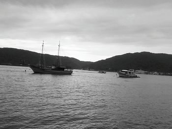 Boats sailing in sea against cloudy sky