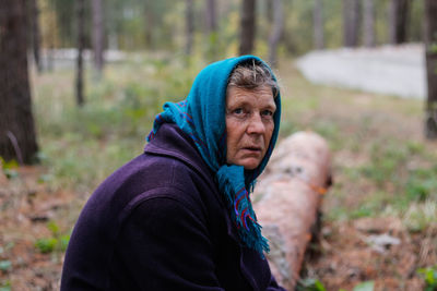 Portrait of russian grandmother senior old woman seating on log in pine autumn forest. old women 